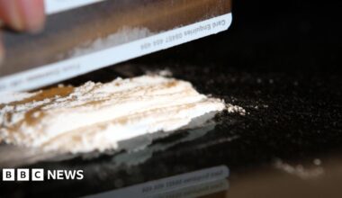 A person cutting up cocaine - only their hand can be seen, as well as the drug