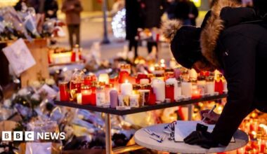 A woman signs a memorial book in front of floral tributes left outside to the victims of a fire at Swiss ski resort