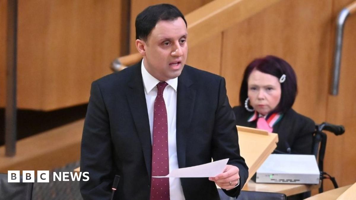 Prime Minister Mark Carney, wearing a black suit jacket, and a white button-up shirt leans his chin on his hands. He has short grey and black hair and is looking away from the camera.