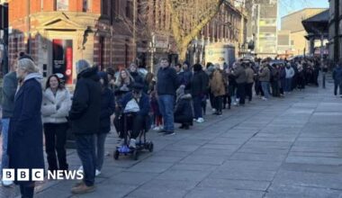A queue of people down a street in Preston. Many are wearing coats and bracing from the cold.