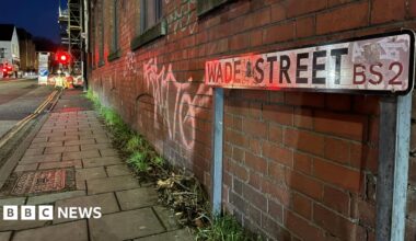 A view of Wade Street. with a street sign in the foreground and roadworks in the distance, there is graffiti on the redbrick wall.