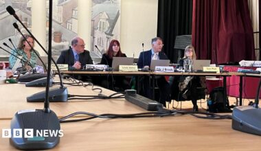 Leading councillors and officers at Westmorland and Furness Council are sitting at a desk with microphones in front of them at a council meeting