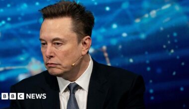 Close up of Elon Musk wearing a suit against a blue background