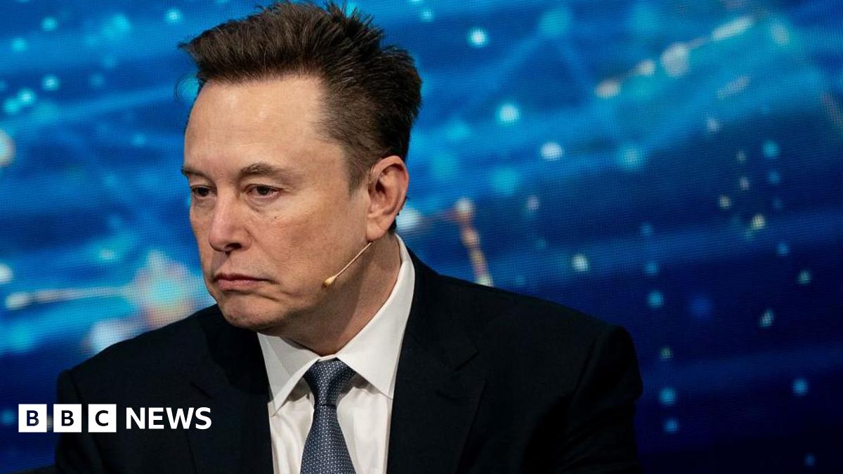 Close up of Elon Musk wearing a suit against a blue background