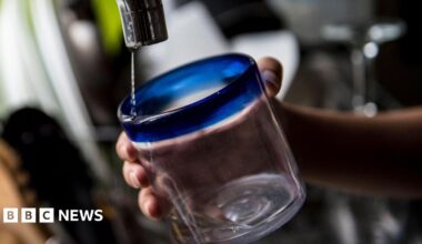 A hand holding a glass under a dripping tap