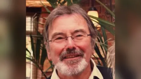 Kent Police A picture of a smiling man with light brown hair, a grey goatee beard and rectangular glasses.