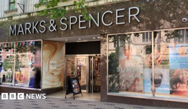 A shop front with a sign in white writing which says Marks & Spencer. There are colourful posters of people in the shop windows.