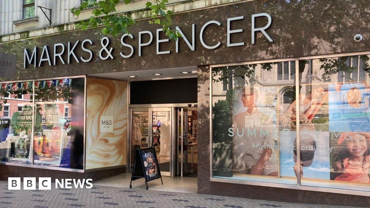 A shop front with a sign in white writing which says Marks & Spencer. There are colourful posters of people in the shop windows.