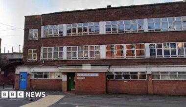 A red brick building. It has many windows. A blue door to the left. And it is a cloudy day.