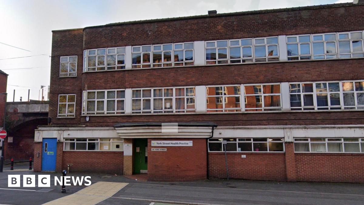 A red brick building. It has many windows. A blue door to the left. And it is a cloudy day.