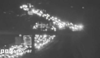 Grainy/black and white blurry image of lots of car lights on a congested M11 going under a bridge