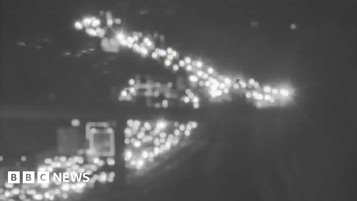 Grainy/black and white blurry image of lots of car lights on a congested M11 going under a bridge