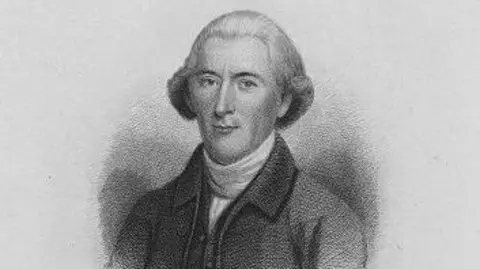 Getty Images A detailed portrait etched in pencil show a man with a straight nose and small mouth wearing a neutral expression. His hair is brushed back from his face and his curled ends cup around his ears. He is wearing a cravat and a high collared coat. 