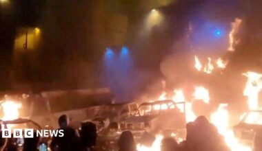 A screen grab of a video shows protesters standing near burning vehicles in the dark in Tehran, Iran.
