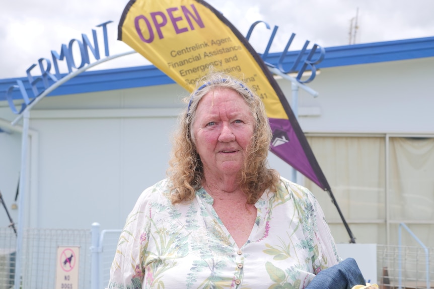 Robyn Cross wearing a floral top in from of a white building and a yellow banner.