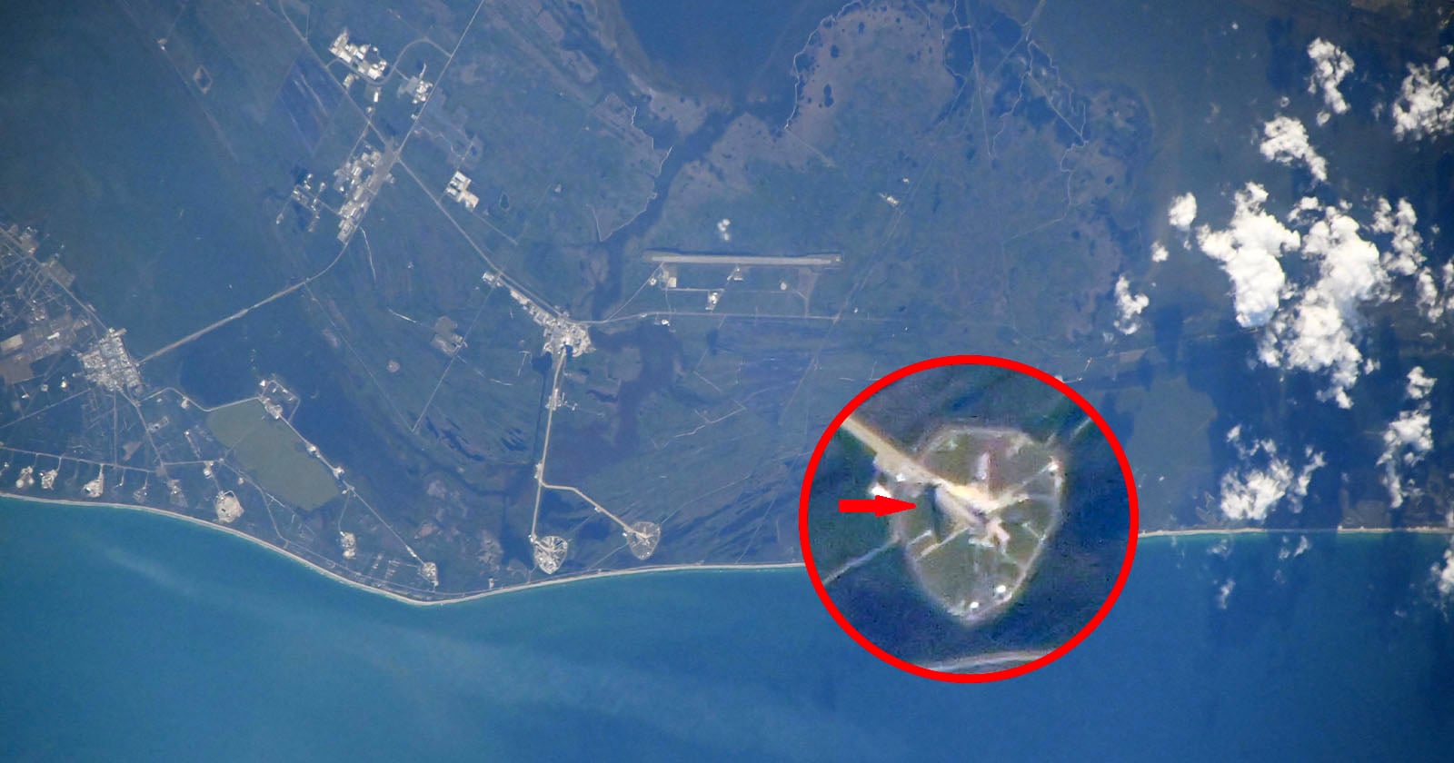 Aerial view of a coastal area with a space launch pad highlighted by a red circle and arrow, showing its location near the shoreline; surrounding land and water are visible.