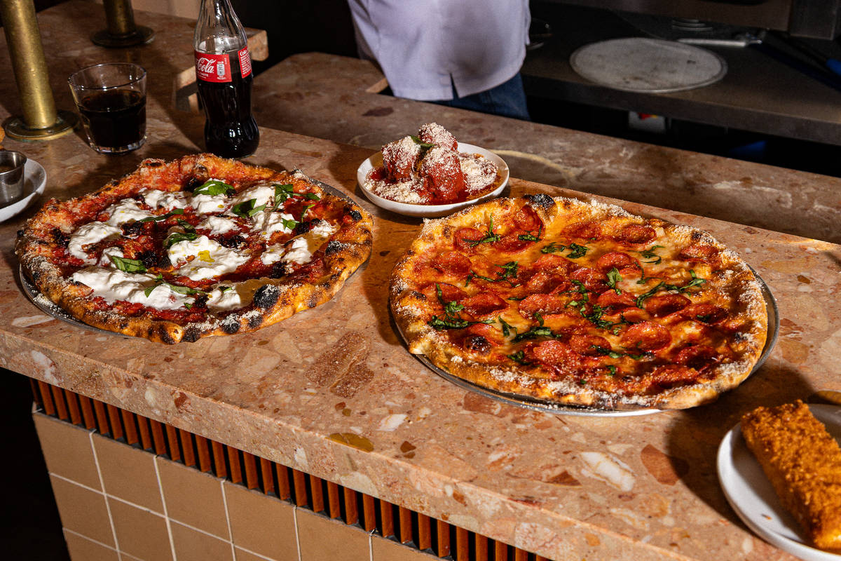 two hefty pizzas presented alongside coke, meatballs, and a deep fried mozarella stick