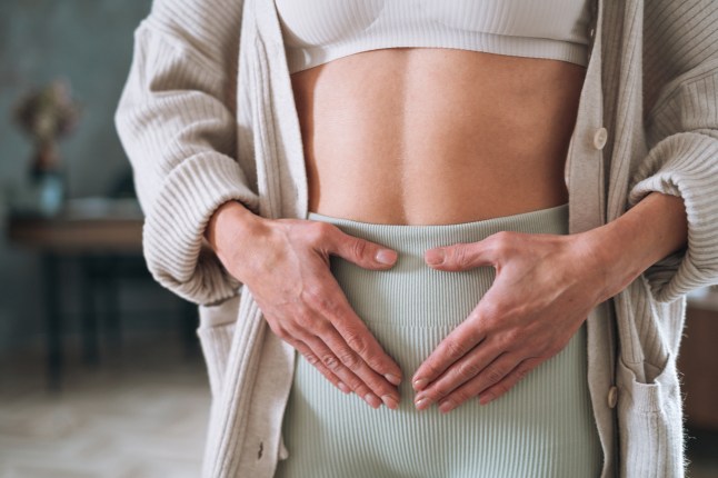 White woman holding her lower abdomen at home, signifying period pain or discomfort.
