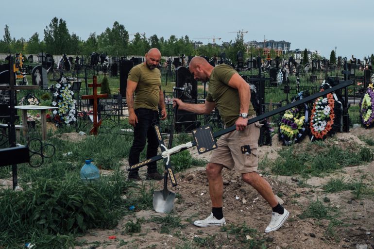 Two volunteers bury the bodies of Ukrainians killed in Russia's attacks on Kyiv in the early months of its full scale invasion [File: Nils Adler/ Al Jazeera]