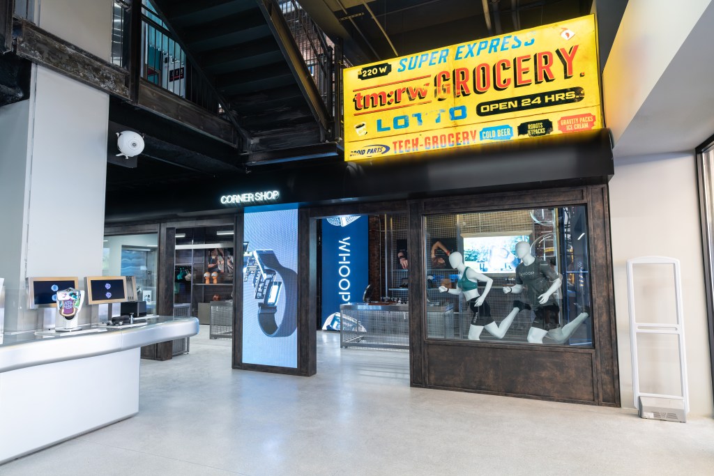 The Corner Shop at tm:rw with a yellow, weathered sign that says "tm:rw GROCERY" with mannequins and smart watch displays inside.