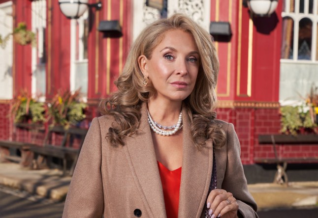Chrissie Watts grins in front of the Queen Vic in EastEnders