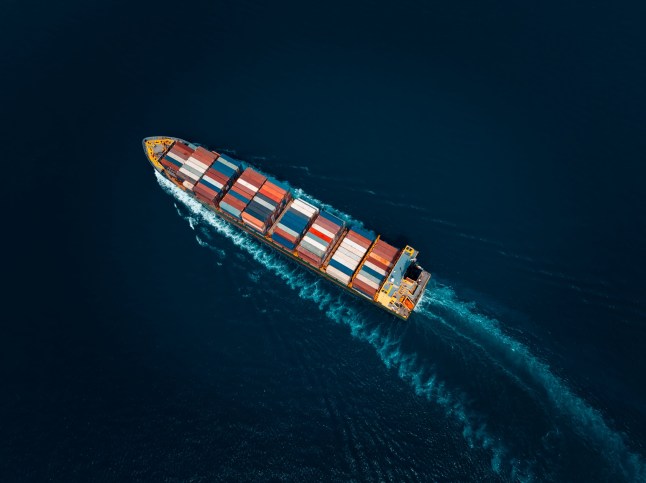 aerial view photograph of large container ship sailing on a deep sea, fully loaded with multi-colored containers, reflecting global maritime transport and logistics, cinematic dark tone process.