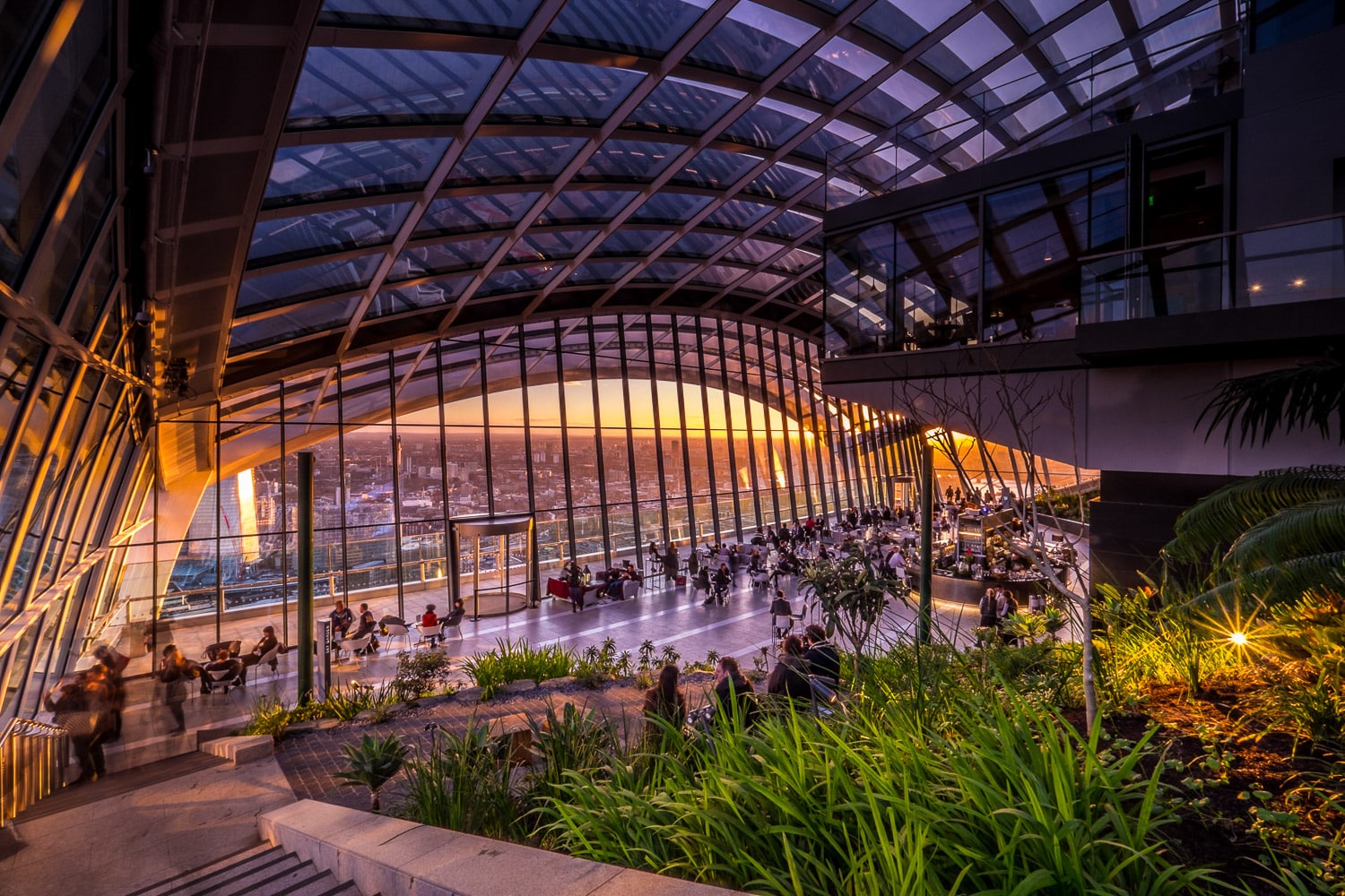 People sitting and standing around in front of the impressive skyline views from the sky garden as golden hour starts