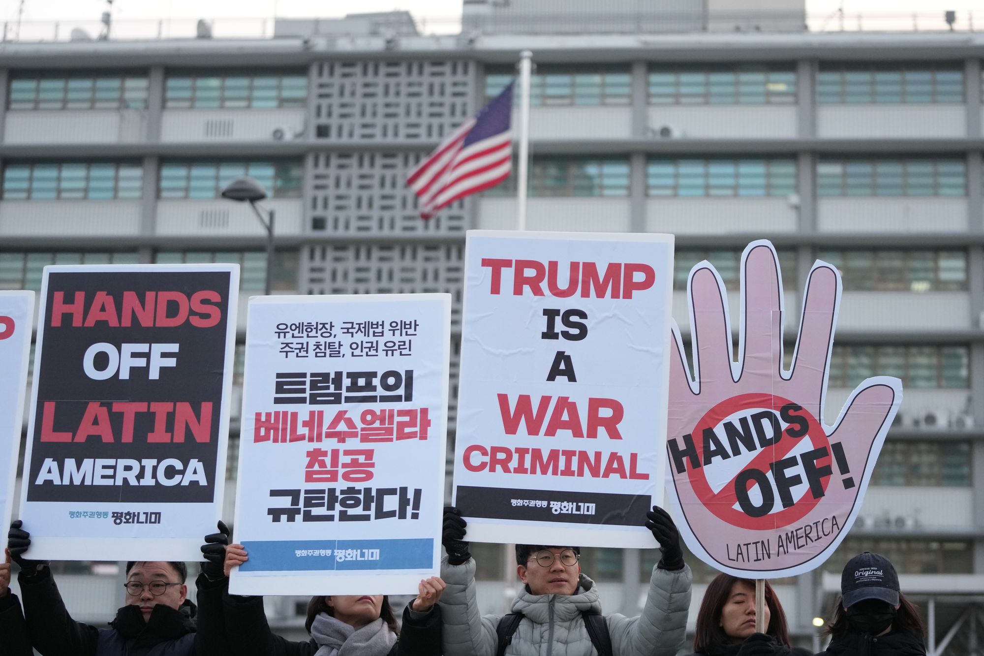 Protesters hold signs denouncing the U.S. military operation against Venezuela, near the U.S. Embassy in Seoul, South Korea, Wednesday