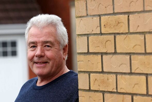 Man smiling and leaning against brick wall