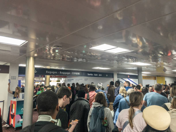 A dense crowd of travelers fills an airport terminal near baggage claim and exit signs, waiting to move through the area.
