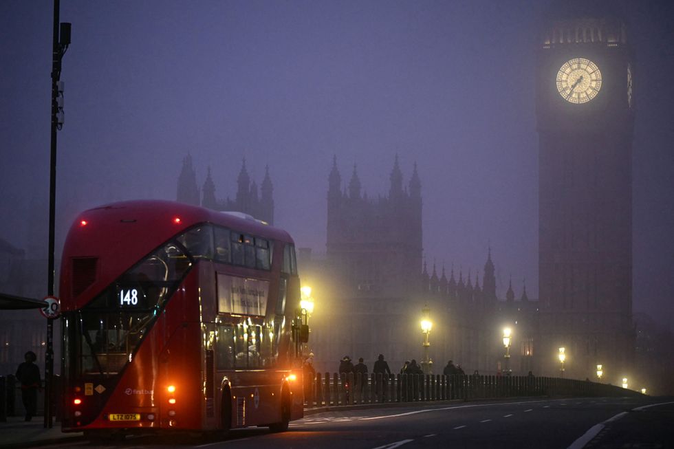 A double-decker bus crosses Westminster Bridge as early morning fog covers the streets of London