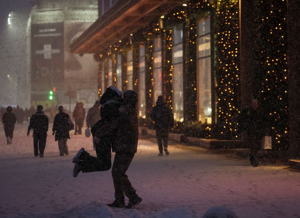 A serviceman hugs a girl as they dance under the snowfall near New Year displays at a shopping mall in Kyiv\u200b