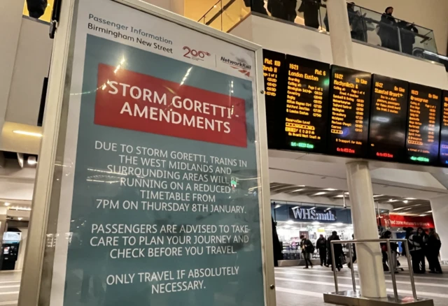 A sign warns that trains are running on a reduced timetable due to Storm Goretti. An electronic train timetable can be seen in the background