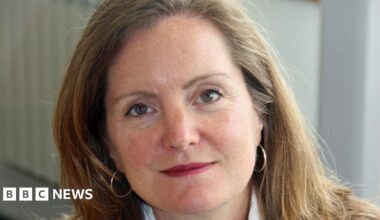 Laura Shoaf has shoulder-length light brown hair. She is wearing small hoop hearings and is slightly smiling towards the camera
