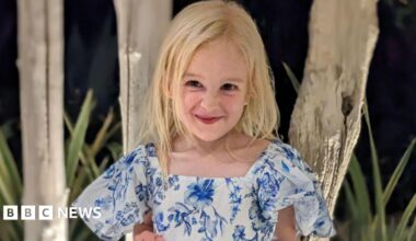 Sofia Hill. She is a young child with long blonde hair. She is wearing a blue and white floral dress and is looking at the camera and smiling.