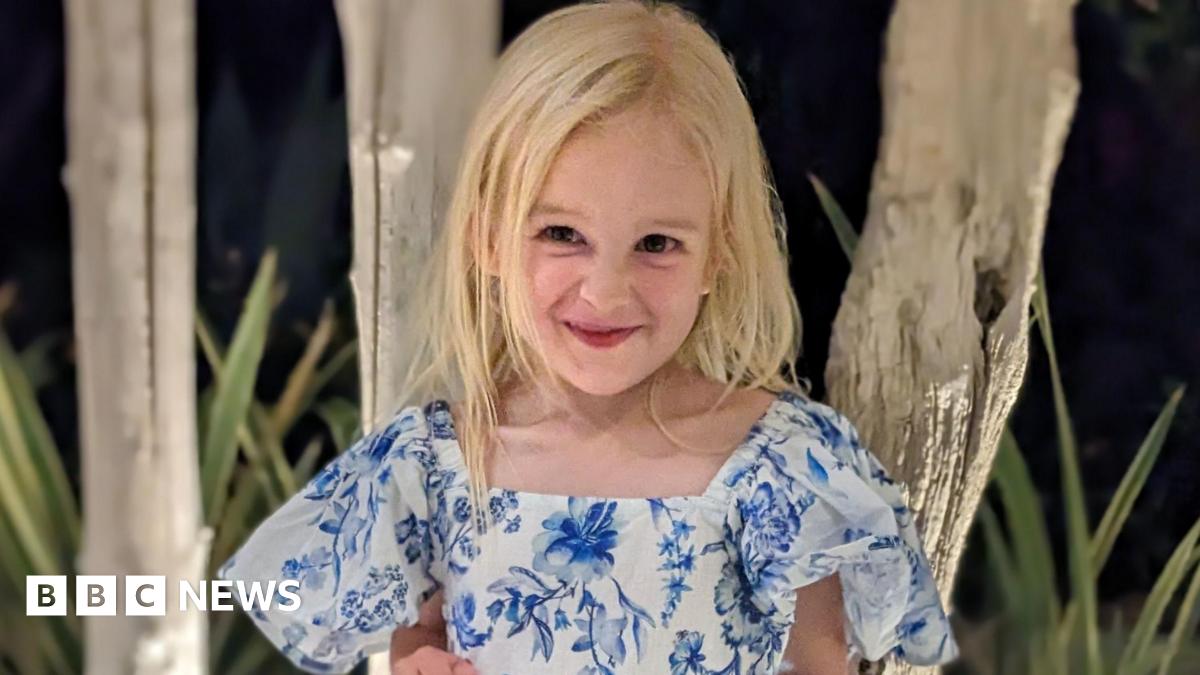 Sofia Hill. She is a young child with long blonde hair. She is wearing a blue and white floral dress and is looking at the camera and smiling.
