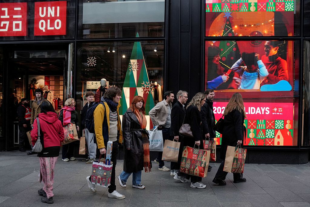 Shoppers walk past popular retail stores along a busy street in central London