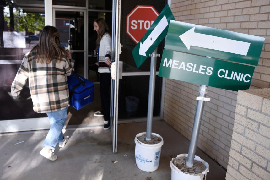 Health department staff members enter the Andrews County Health Department measles clinic carrying doses of the measles, mumps and rubella vaccine on April 8, 2025, in Andrews, Texas.
