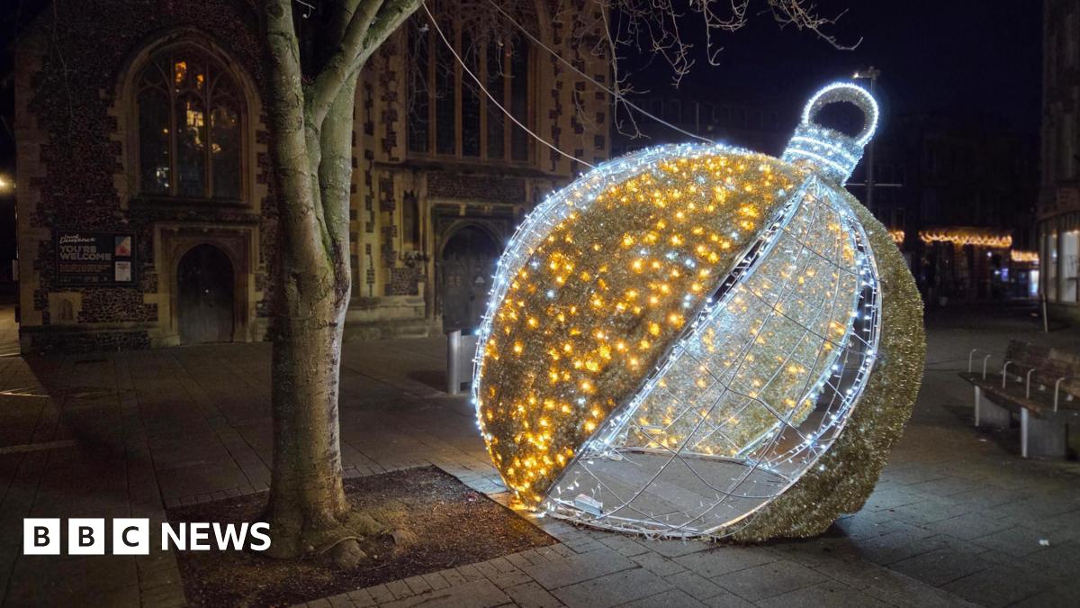 One of the town's Christmas lights - a large silver and gold bauble - is on the ground next to a tree. A church is in the background.