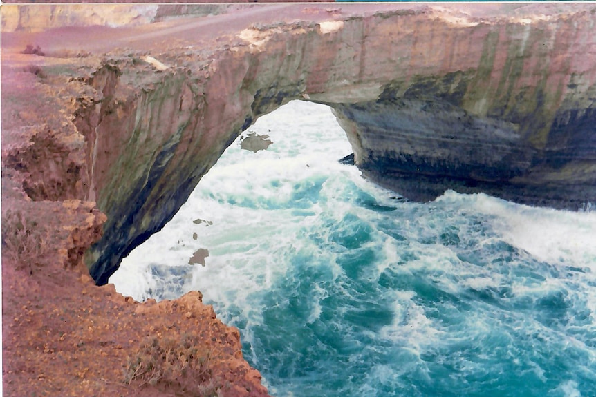 A large limestone bridge in ocean with small pieces of rock falling off