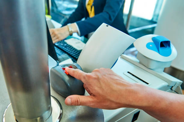 A traveler places a finger on a biometric scanner at an airport immigration counter while an officer works in the background.