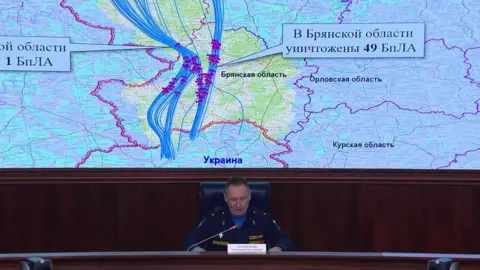 Russian defence ministry A Russian defence ministry official sits in front of a large screen which shows a map, marked with the the alleged flight paths of the drones Russia says Ukraine launched at one of Putin's residences. 