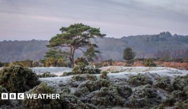 A young boy and girl, wearing blue and pink clothes, patting down snow on a snowman bigger than them