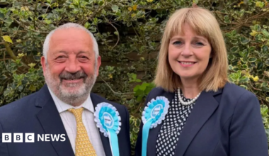 Marcus Lapsa and Jackie Gardiner look at the camera. They are wearing dark blue blazers and light blue and white Reform UK rosettes.