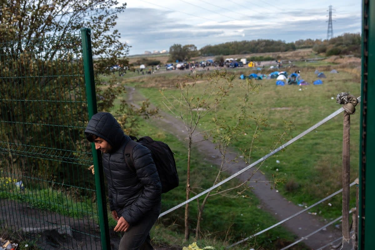 A man passes through a gap in a security fence near a migrant camp on October 31, 2025 in Loon-Plage, France. (Getty Images)