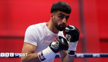 Adam Azim holds up his hands and is wearing a white t-shirt with black boxing gloves