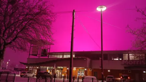 GLMCC Pink sky over a Morrisons supermarket in Small Heath area of Birmingham. The supermarket is lit with snow seen in its car park and a bright street light. 
