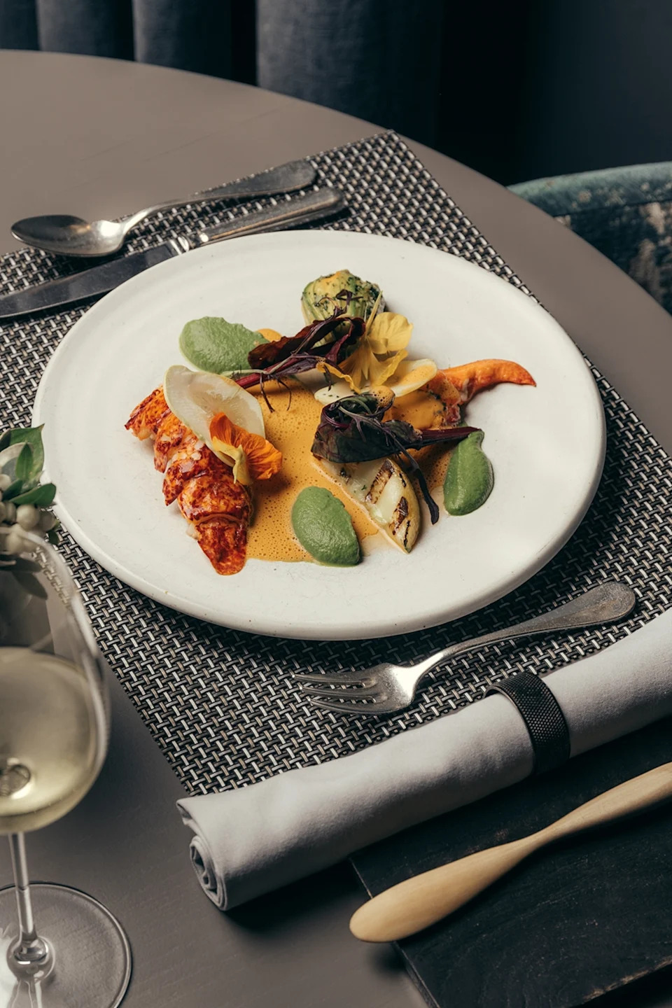 A plate of fine-dining-style lobster, stuffed courgette flower and lobster bisque on a sleek table.