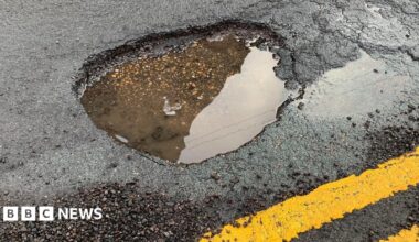 Prime Minister Mark Carney, wearing a black suit jacket, and a white button-up shirt leans his chin on his hands. He has short grey and black hair and is looking away from the camera.