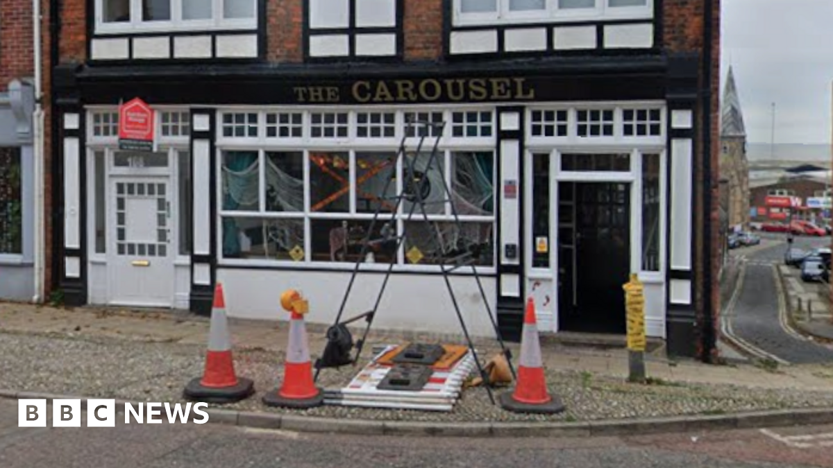 A Google image of a pub. It is a black and white painted building. Three traffic cones are in front of it.